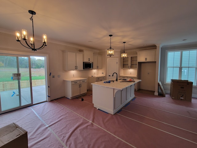 kitchen featuring white cabinetry, sink, an island with sink, crown molding, and pendant lighting