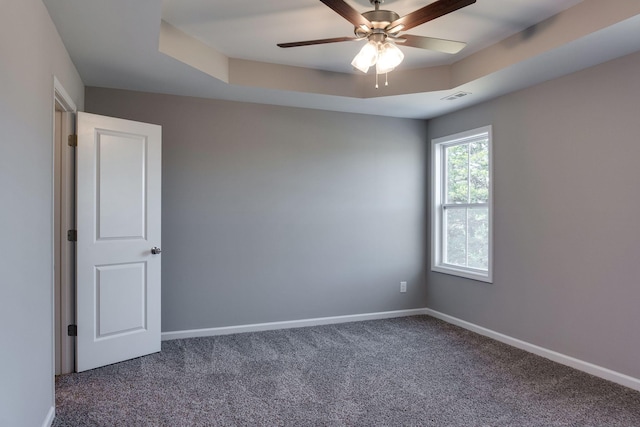 spare room with ceiling fan, dark carpet, and a raised ceiling