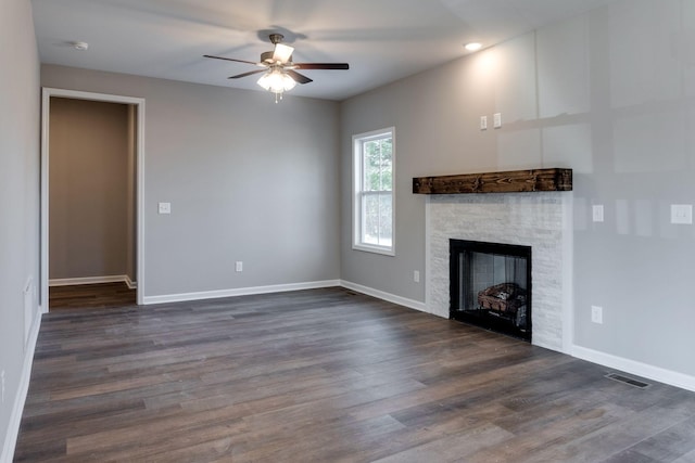 unfurnished living room with ceiling fan, dark hardwood / wood-style flooring, and a stone fireplace