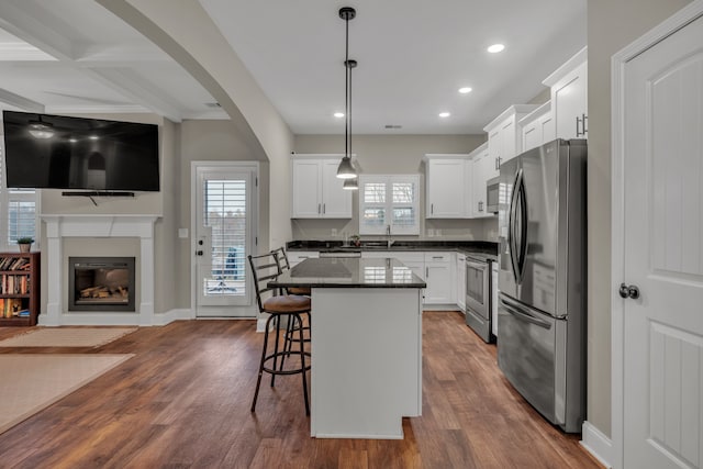 kitchen featuring pendant lighting, hardwood / wood-style floors, a kitchen island, white cabinetry, and appliances with stainless steel finishes