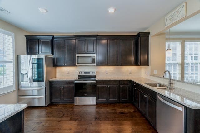 kitchen featuring stainless steel appliances, dark hardwood / wood-style floors, sink, and light stone counters