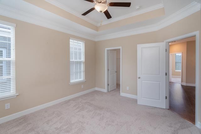 unfurnished bedroom with a raised ceiling, light carpet, ceiling fan, and crown molding