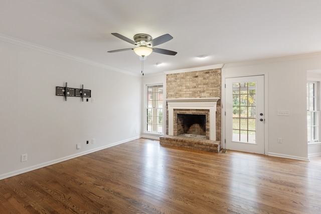 unfurnished living room featuring crown molding, wood-type flooring, ceiling fan, and a brick fireplace