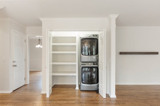 clothes washing area featuring wood-type flooring, crown molding, and stacked washer / drying machine