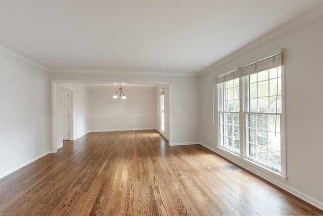 spare room featuring a wealth of natural light, wood-type flooring, a chandelier, and crown molding