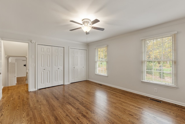 unfurnished bedroom featuring hardwood / wood-style floors, ceiling fan, crown molding, and two closets