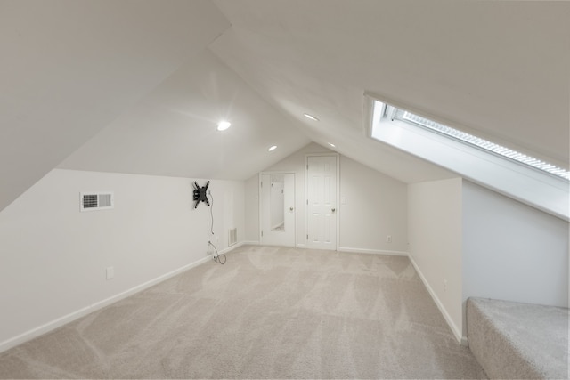 additional living space featuring vaulted ceiling with skylight and light colored carpet