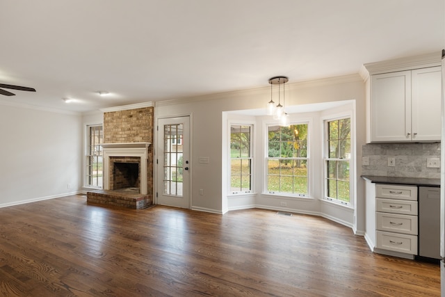 unfurnished living room with dark wood-type flooring, ceiling fan, ornamental molding, and a brick fireplace