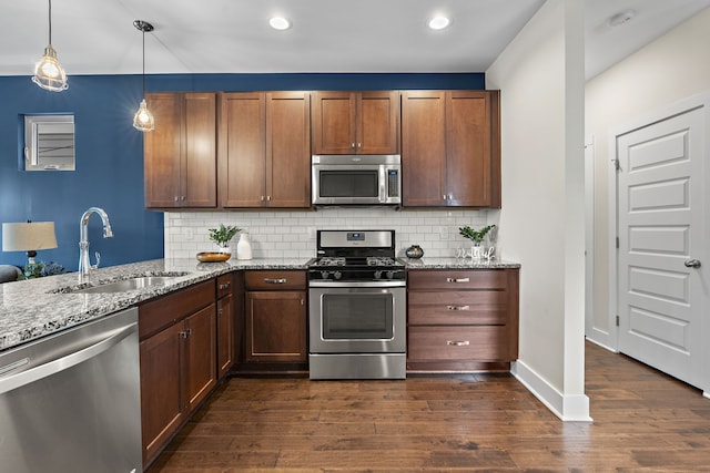 kitchen with stainless steel appliances, sink, light stone countertops, hanging light fixtures, and dark wood-type flooring