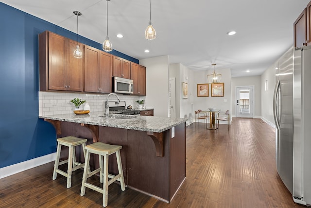 kitchen with stainless steel appliances, light stone countertops, dark hardwood / wood-style floors, hanging light fixtures, and decorative backsplash