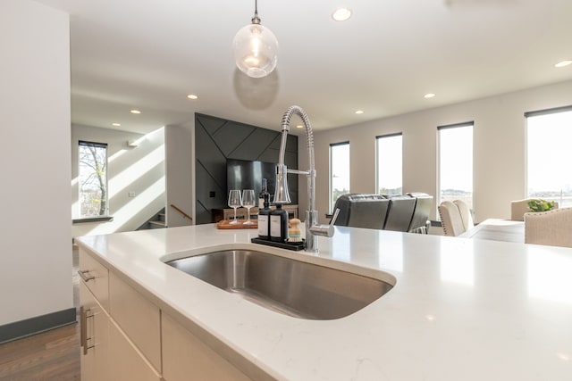 kitchen featuring dark hardwood / wood-style flooring, hanging light fixtures, sink, and light stone counters