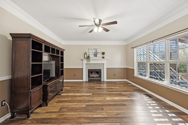 living room with ceiling fan, crown molding, dark wood-type flooring, and a tiled fireplace