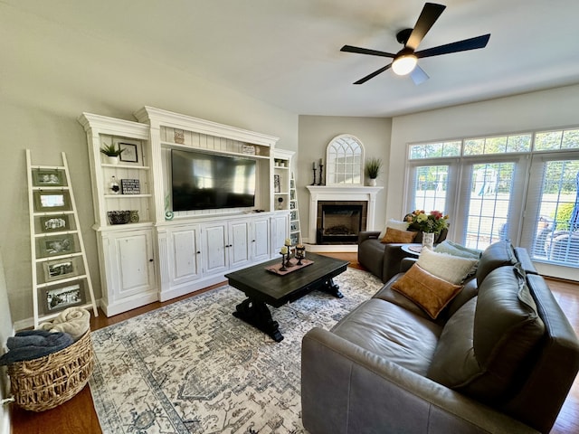 living room with built in features, wood-type flooring, and ceiling fan