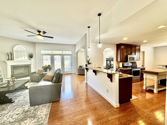 kitchen with stainless steel appliances, dark hardwood / wood-style floors, pendant lighting, light stone countertops, and a breakfast bar