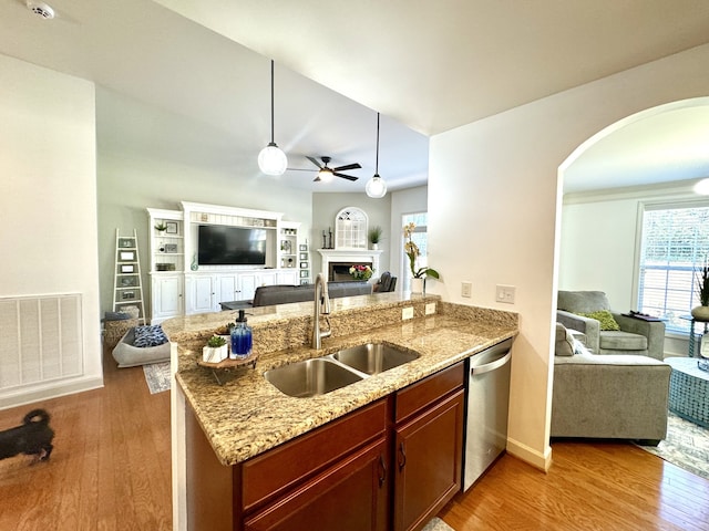 kitchen featuring dishwasher, sink, light stone countertops, light wood-type flooring, and decorative light fixtures