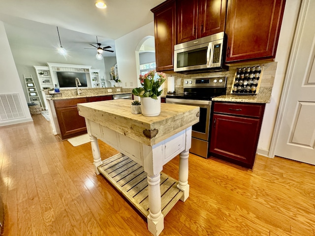 kitchen featuring stainless steel appliances, light stone counters, kitchen peninsula, ceiling fan, and light hardwood / wood-style flooring