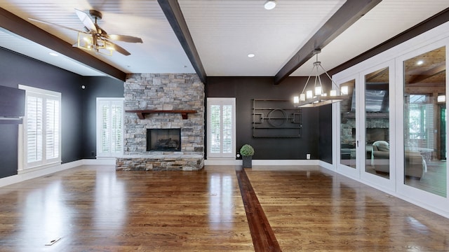 unfurnished living room with a fireplace, ceiling fan with notable chandelier, dark wood-type flooring, and beam ceiling