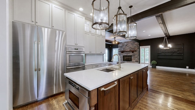 kitchen with stainless steel appliances, dark hardwood / wood-style floors, a kitchen island with sink, white cabinets, and pendant lighting