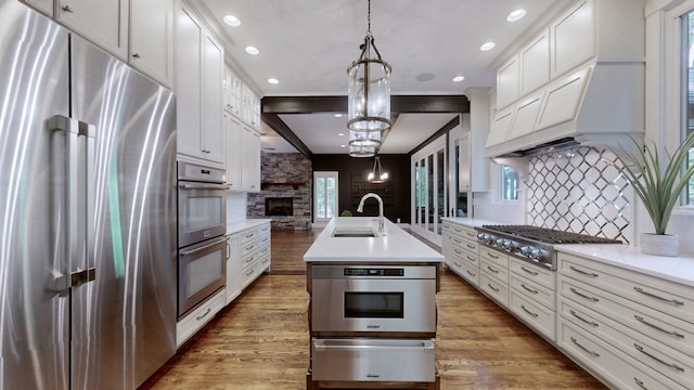 kitchen with sink, appliances with stainless steel finishes, an island with sink, hanging light fixtures, and white cabinets