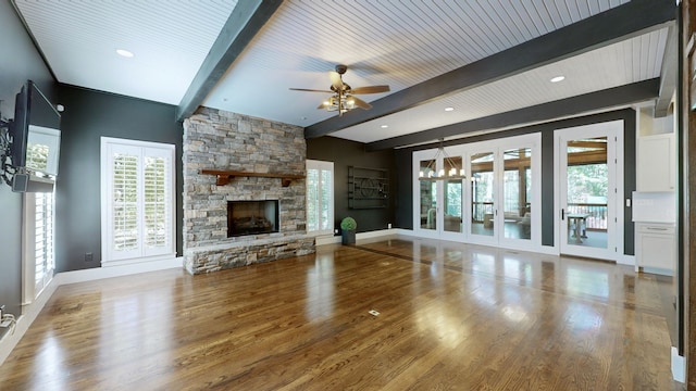 unfurnished living room featuring a stone fireplace, beam ceiling, ceiling fan with notable chandelier, and wood-type flooring