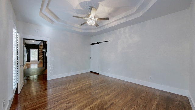 unfurnished room with dark wood-type flooring, a barn door, ceiling fan, and a raised ceiling