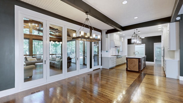 kitchen featuring hanging light fixtures, a kitchen island with sink, beamed ceiling, dark hardwood / wood-style floors, and white cabinetry