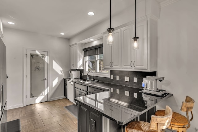 kitchen with white cabinetry, pendant lighting, dishwasher, kitchen peninsula, and dark stone countertops