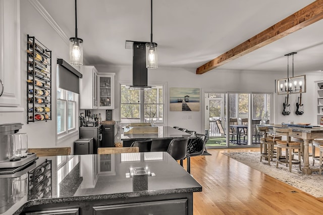 kitchen featuring island range hood, hanging light fixtures, beamed ceiling, white cabinetry, and light hardwood / wood-style flooring