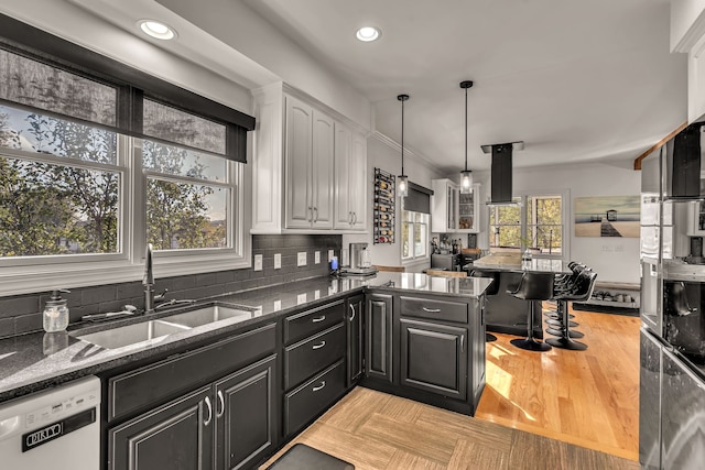 kitchen with light hardwood / wood-style floors, white dishwasher, kitchen peninsula, decorative backsplash, and sink