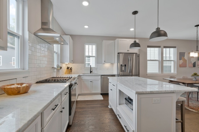 kitchen with white cabinetry, appliances with stainless steel finishes, wall chimney range hood, and light stone counters