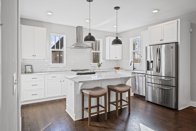 kitchen with wall chimney exhaust hood, white cabinetry, appliances with stainless steel finishes, and a kitchen island