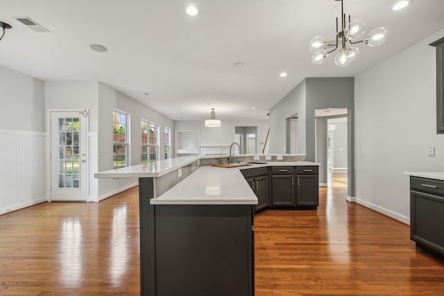 kitchen with sink, pendant lighting, wood-type flooring, and a kitchen island with sink