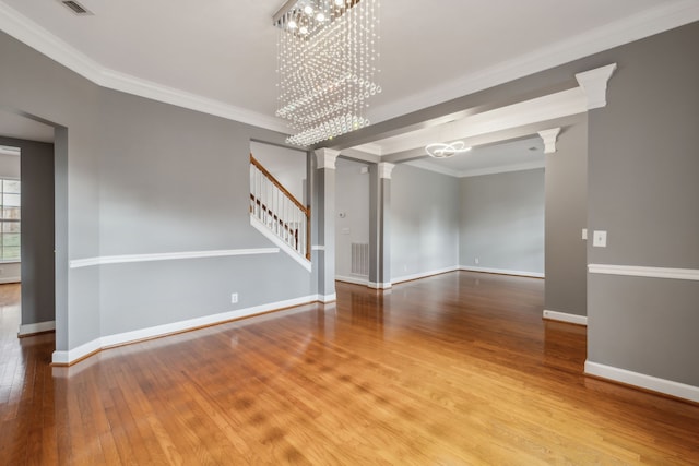 unfurnished room with hardwood / wood-style flooring, a notable chandelier, ornate columns, and ornamental molding