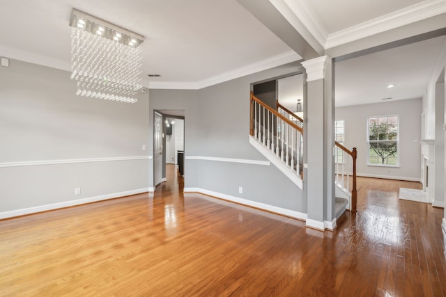 spare room featuring a chandelier, wood-type flooring, ornate columns, and crown molding