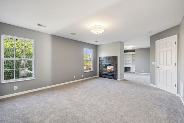 unfurnished living room featuring built in features, a tiled fireplace, and light colored carpet