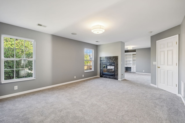 unfurnished living room with a tiled fireplace, light carpet, and built in features