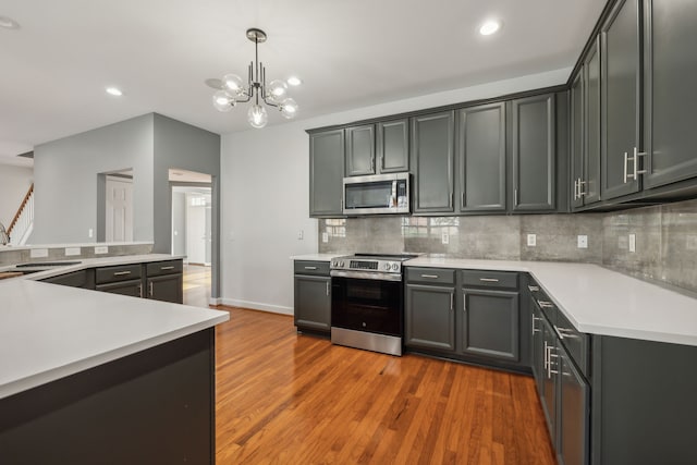 kitchen with a notable chandelier, gray cabinets, light wood-type flooring, appliances with stainless steel finishes, and decorative light fixtures