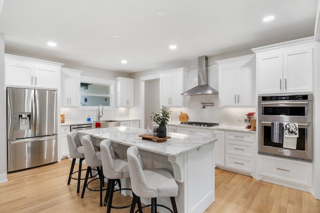 kitchen with stainless steel appliances, white cabinetry, light hardwood / wood-style floors, wall chimney exhaust hood, and a center island