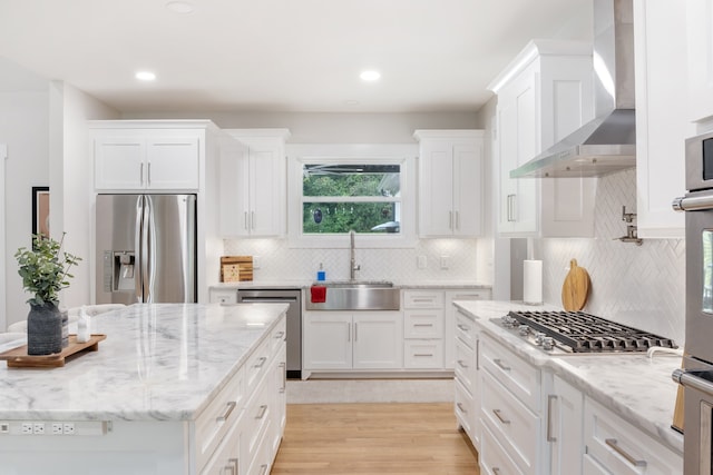 kitchen with stainless steel appliances, light hardwood / wood-style floors, sink, wall chimney exhaust hood, and white cabinets