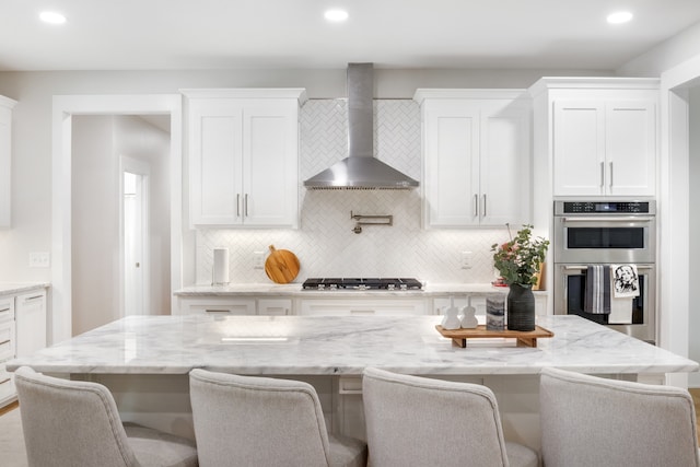 kitchen with wall chimney range hood, white cabinets, a breakfast bar area, and stainless steel appliances