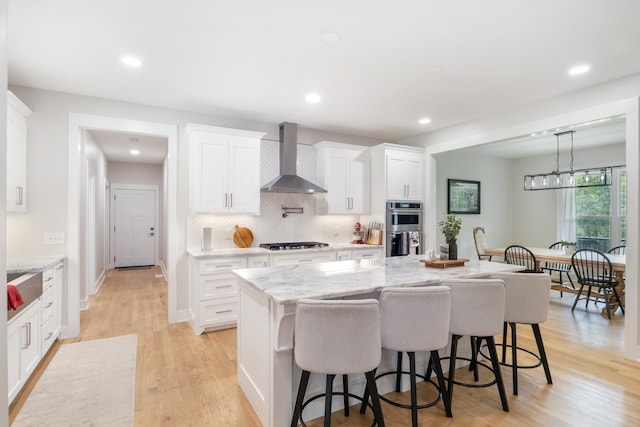 kitchen with wall chimney exhaust hood, gas stovetop, light hardwood / wood-style flooring, a center island, and white cabinets