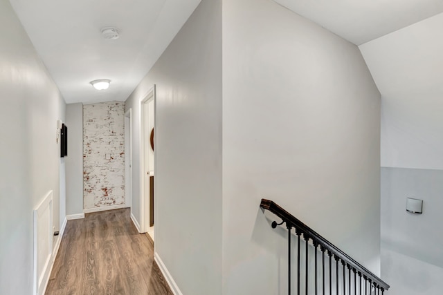 corridor with baseboards, wood finished floors, and an upstairs landing