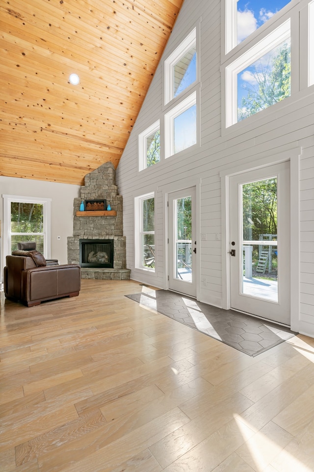 unfurnished living room with light wood-type flooring, high vaulted ceiling, a wealth of natural light, and a stone fireplace