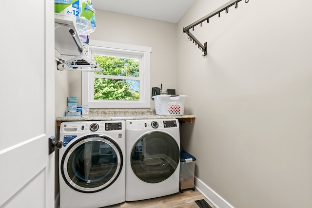 clothes washing area with washer and clothes dryer and light wood-type flooring