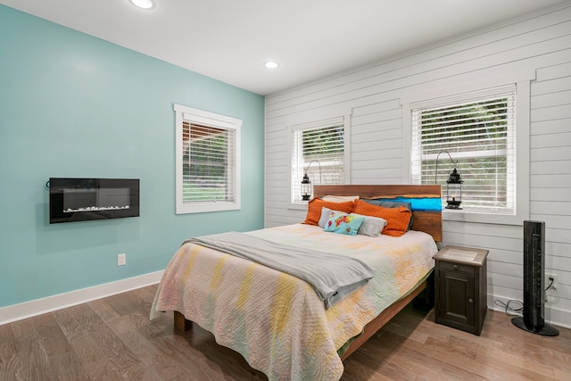 bedroom with multiple windows, wooden walls, and hardwood / wood-style floors