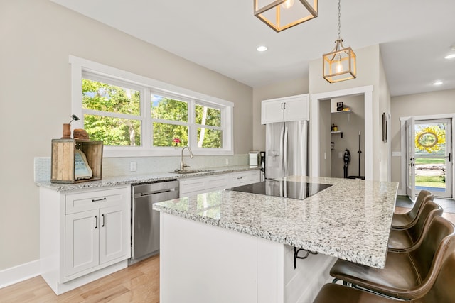 kitchen featuring white cabinets, hanging light fixtures, light hardwood / wood-style flooring, a kitchen island, and stainless steel appliances