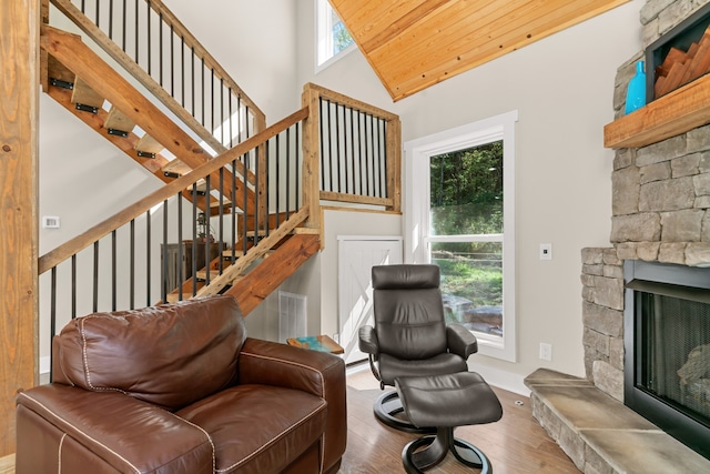 sitting room featuring a stone fireplace, a healthy amount of sunlight, hardwood / wood-style floors, and wood ceiling