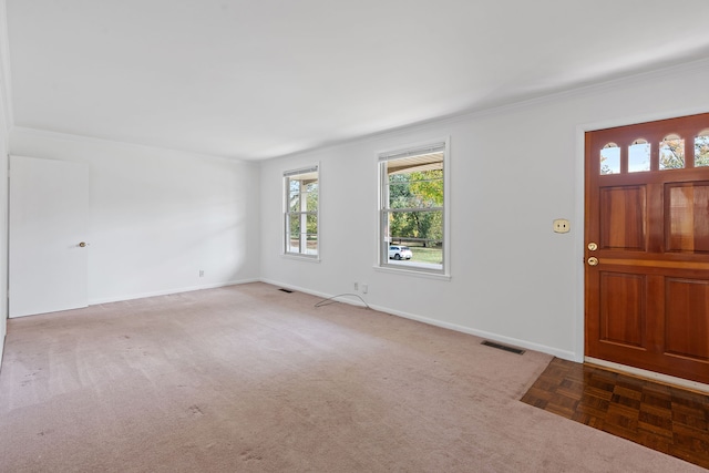 foyer entrance with ornamental molding and dark colored carpet