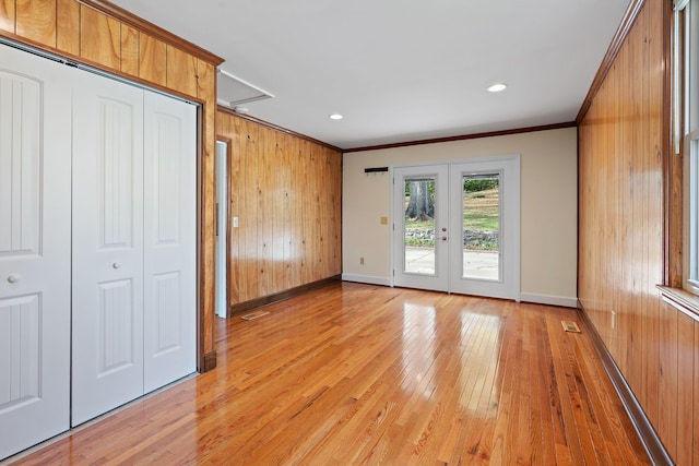 interior space featuring wooden walls, french doors, ornamental molding, and light hardwood / wood-style flooring