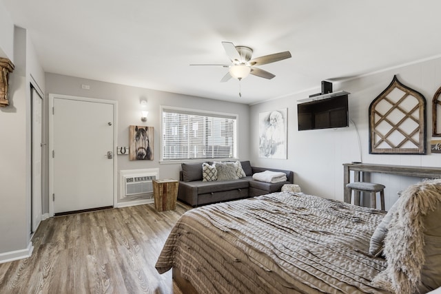 bedroom with a wall mounted air conditioner, light hardwood / wood-style flooring, ceiling fan, and a closet